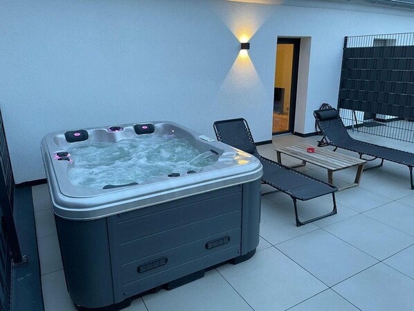 Een hottub met een tafel en stoelen, een overdekt terras en een zwarte metalen hek.