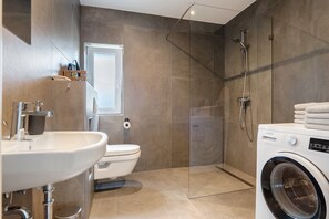 Een moderne badkamer met een wastafel, toilet, douchecabine met glazen wanden en een voorlader wasmachine.