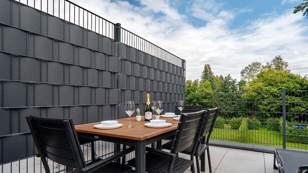 Une terrasse avec une table dressée pour quatre personnes, des chaises, une bouteille de champagne et une vue sur un paysage verdoyant.