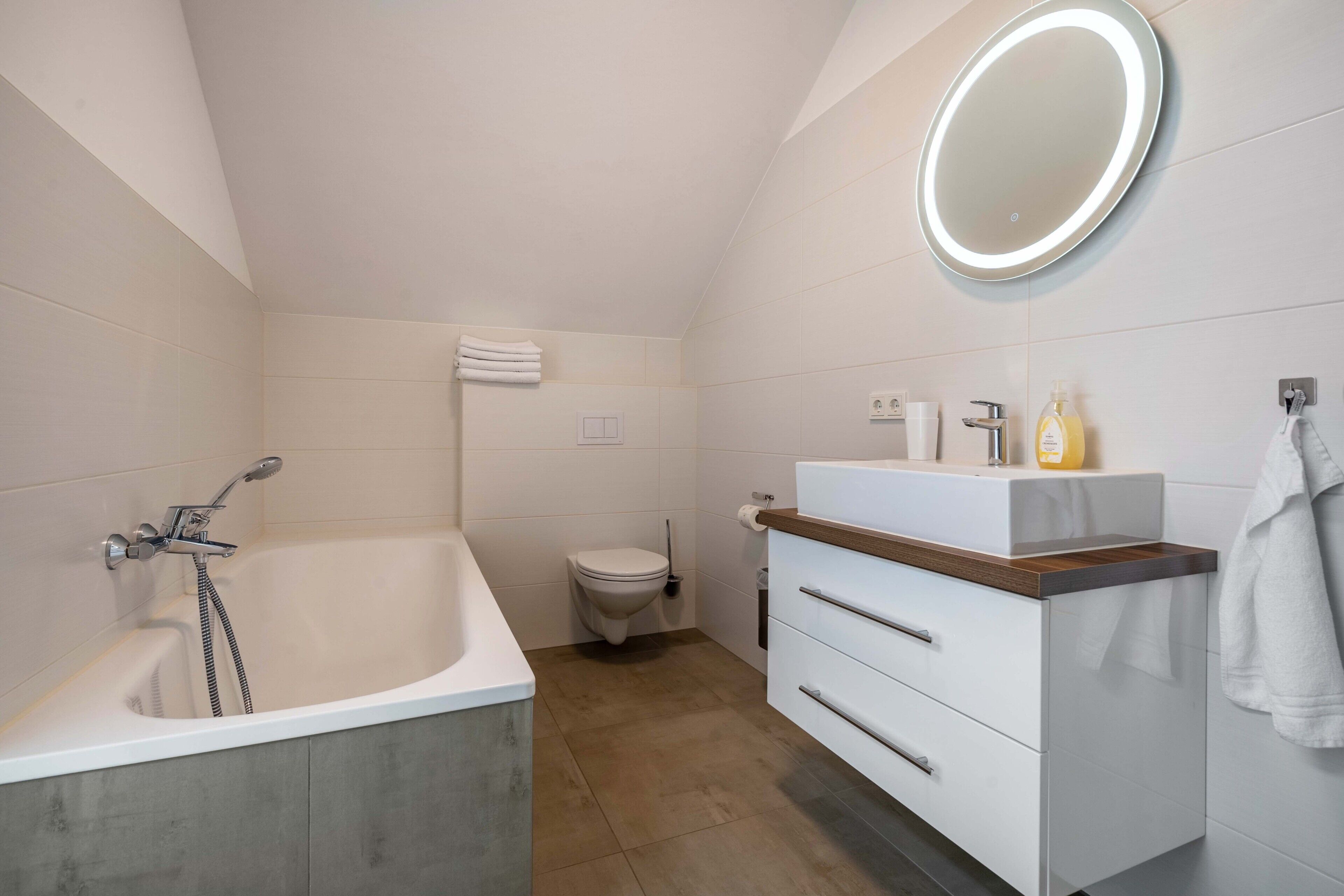 A modern bathroom with a bathtub, toilet, vanity, and a mirror with a light.