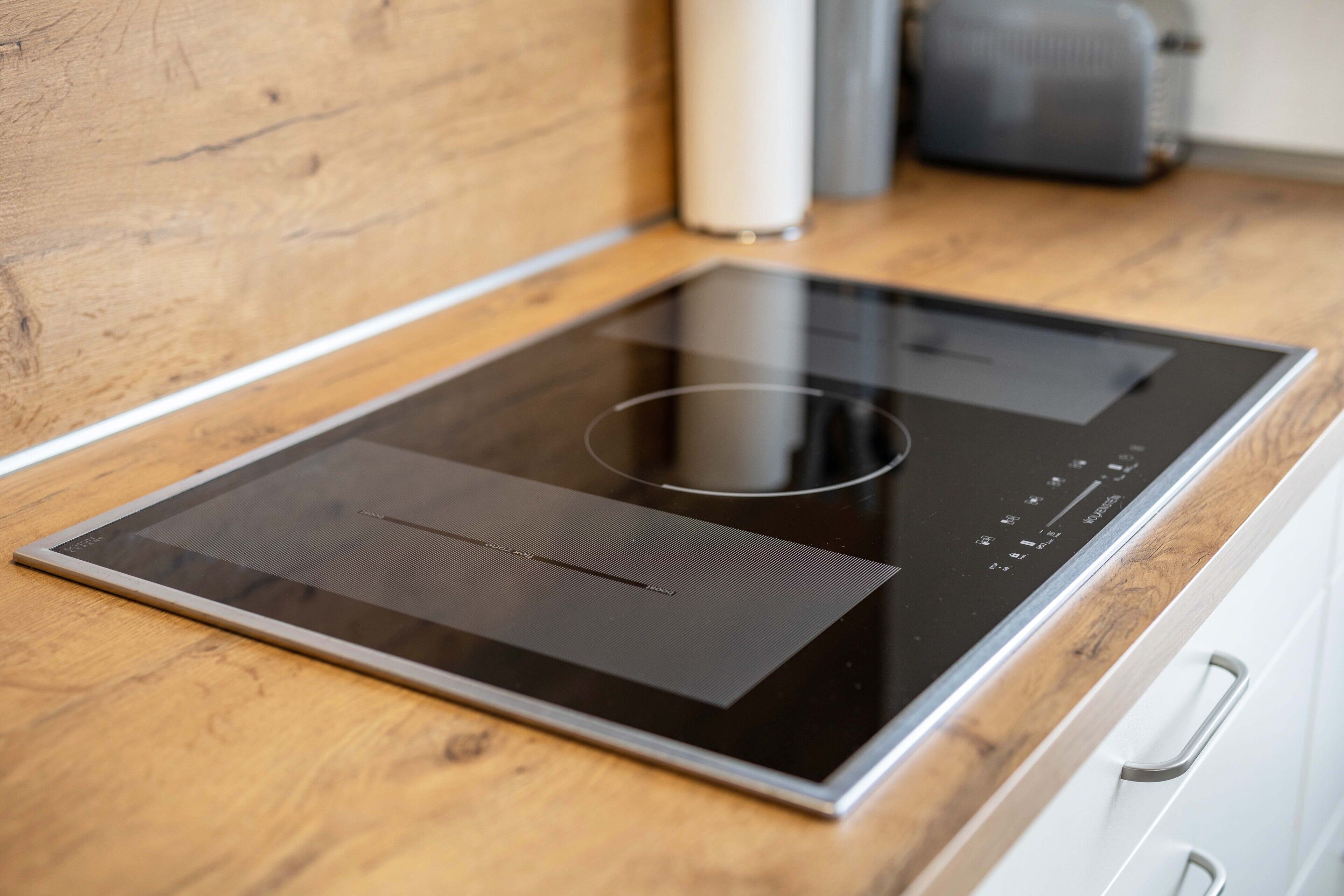 A modern kitchen with a built-in induction cooktop, a wooden countertop, and a white cabinet.