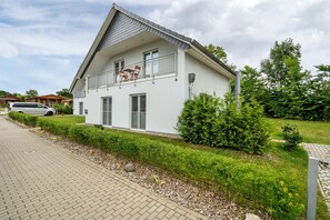 A modern two-story building with a balcony, a paved driveway, and a well-maintained garden.