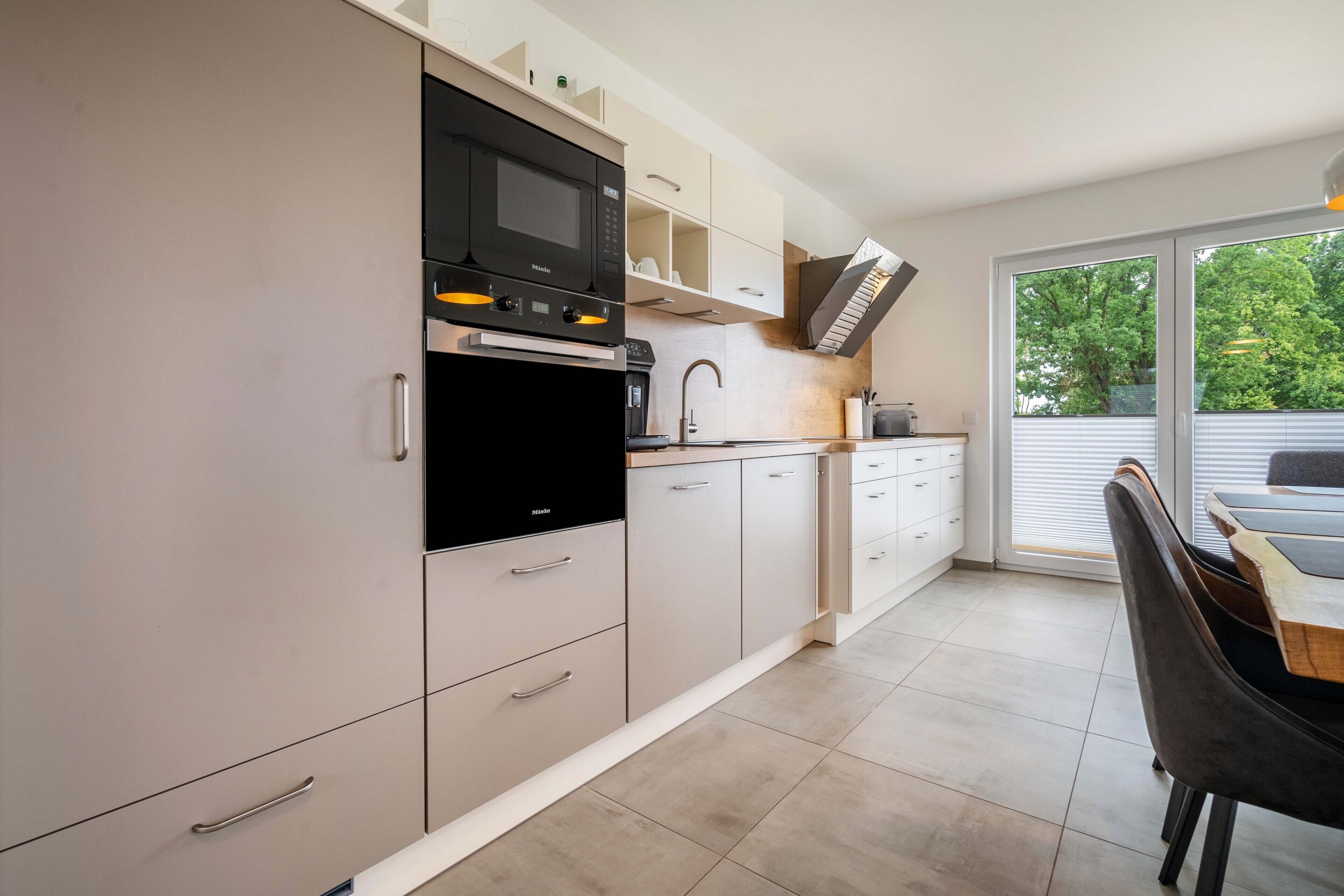 Eine moderne Küche mit eingebauter Mikrowelle, Backofen und Spüle, ein Essbereich mit Tisch und Stühlen sowie eine Glastür, die auf einen Balkon führt.