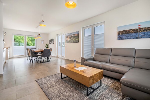 A modern living room with a sofa, a wooden coffee table, and a dining area with chairs and a table.