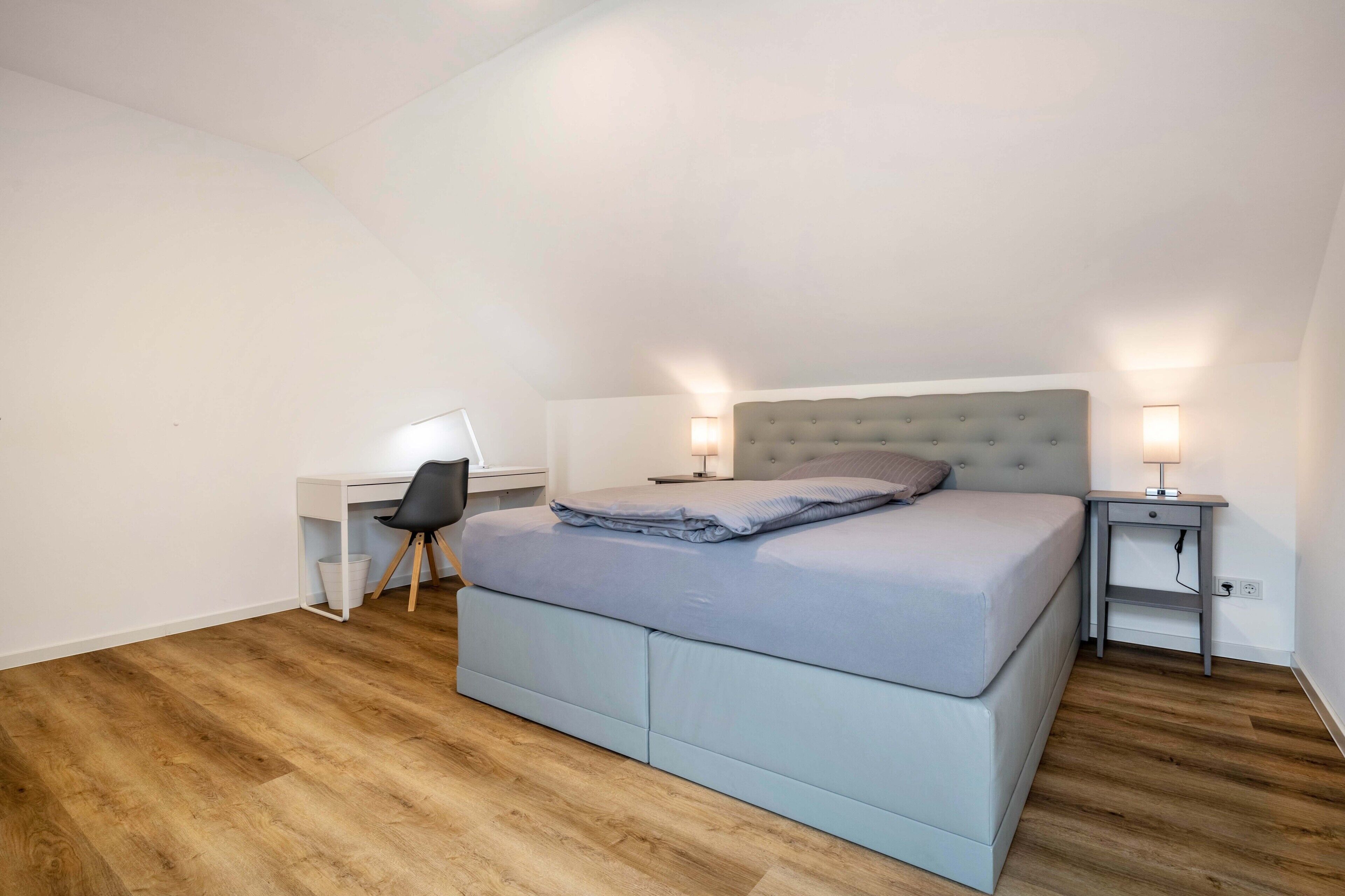 Ein Schlafzimmer mit Bett, Schreibtisch, Stuhl und Nachttischlampen.