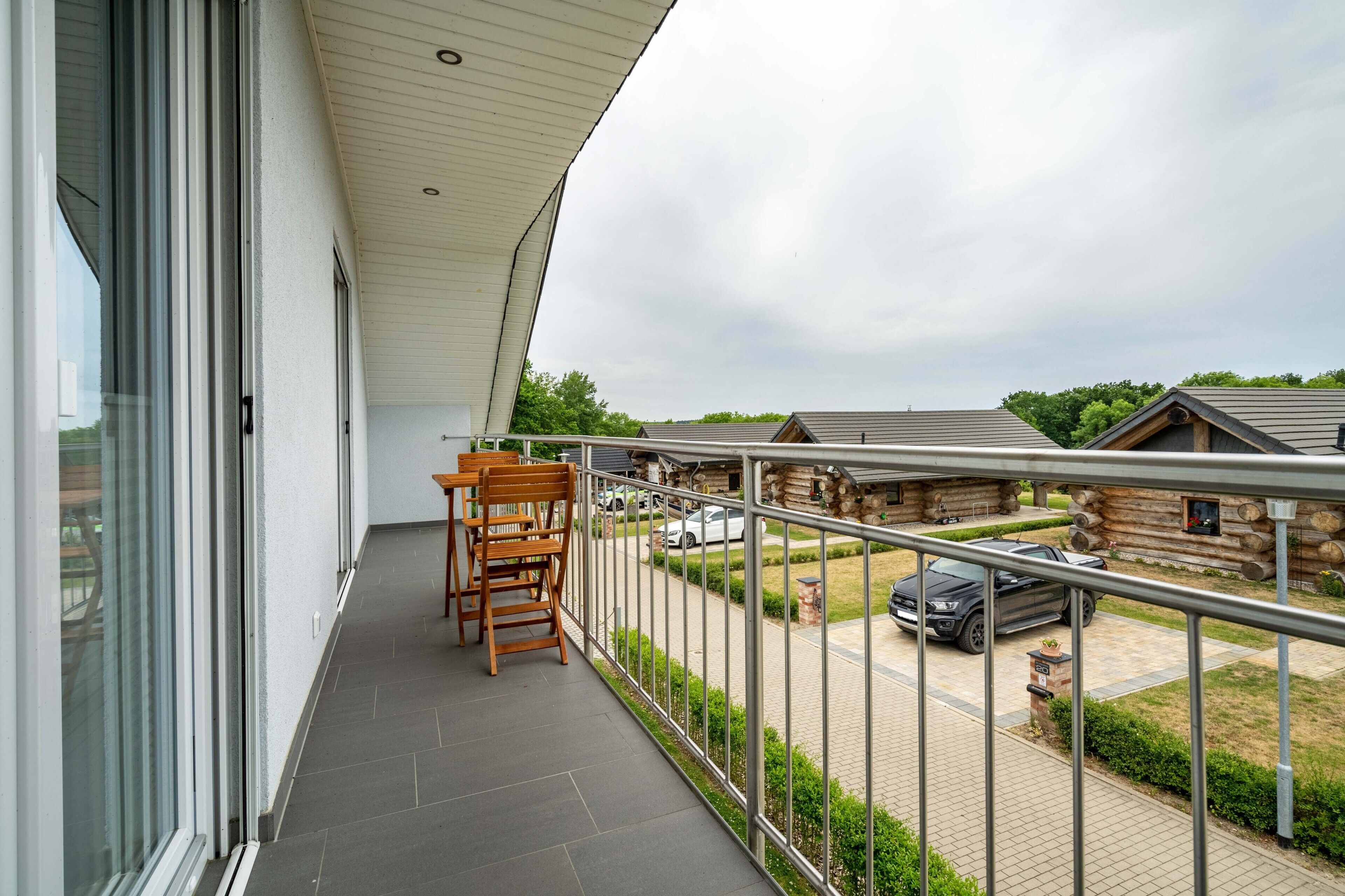 A balcony with a view of a driveway, a parked car, and a log cabin structure.