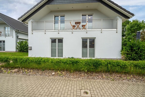 A two-story residential building with a balcony, large windows, and a paved driveway.