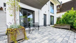 Eine Terrasse mit Sitzgelegenheit, ein großer Pflanzkübel mit Pflanzen und ein Gebäude im modernen Stil.