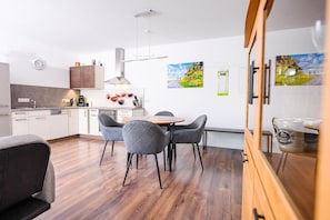 Eine moderne Küche mit weißen Schränken, ein Essbereich mit grau bezogenen Stühlen und ein Holzboden.