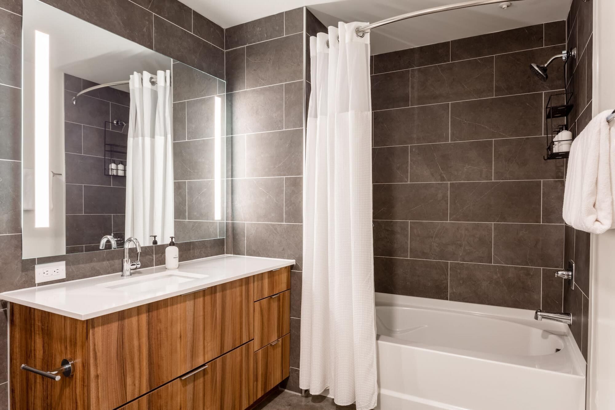 A modern bathroom with a wooden vanity, a large mirror, a bathtub, and a shower curtain.