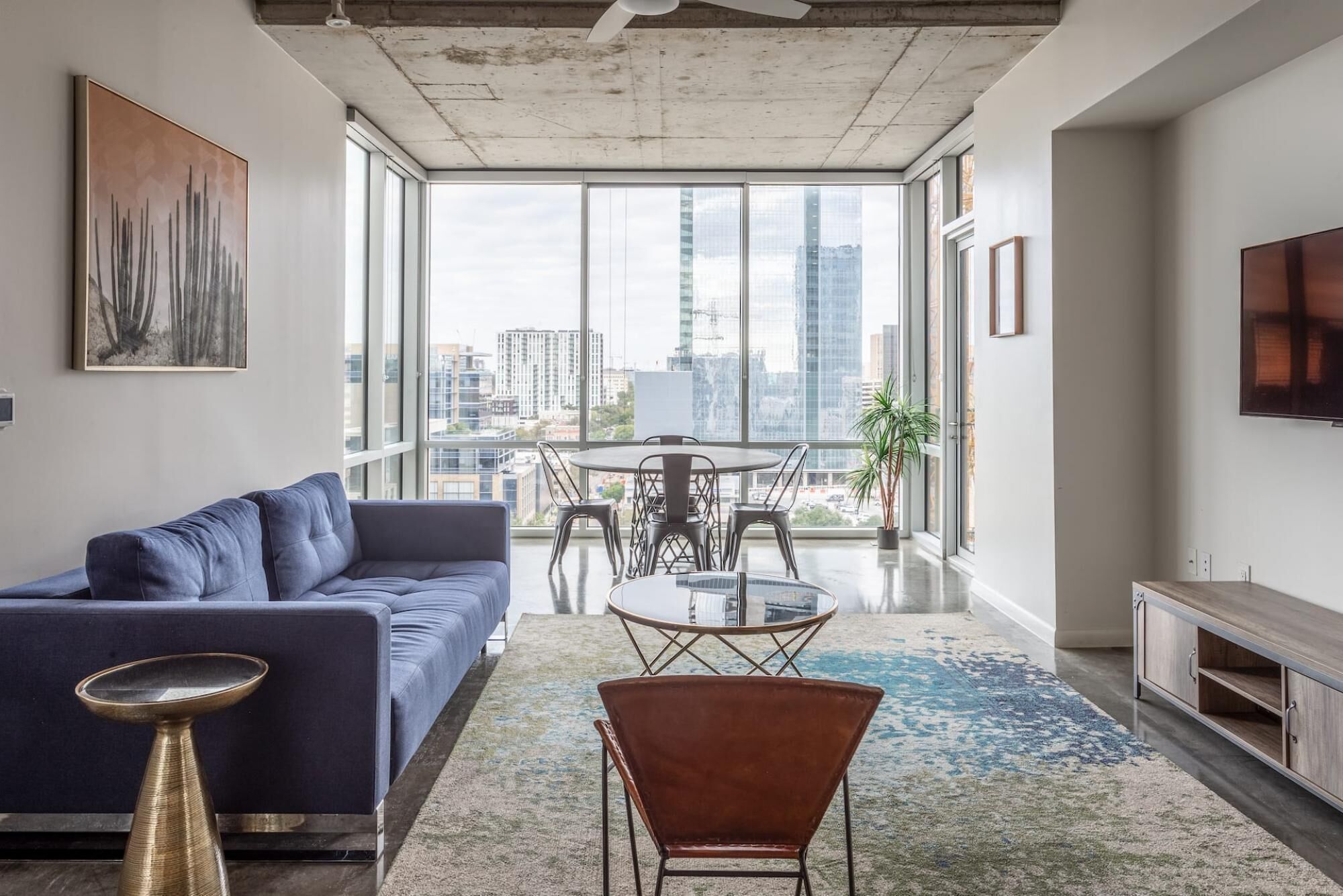 A modern living room with a blue sofa, a glass coffee table, and a patterned rug.