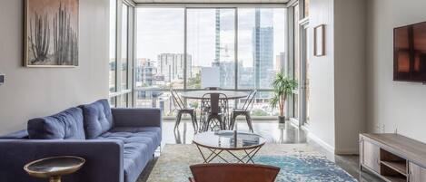 A modern living room with a blue sofa, a glass coffee table, and a patterned rug.