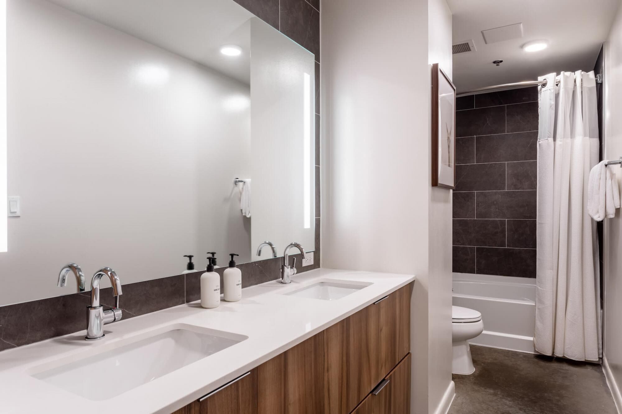 A modern bathroom with two sinks, a large mirror, and a shower area.