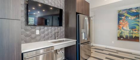 A modern kitchen with a stainless steel refrigerator, a built-in dishwasher, and a large window above the sink.
