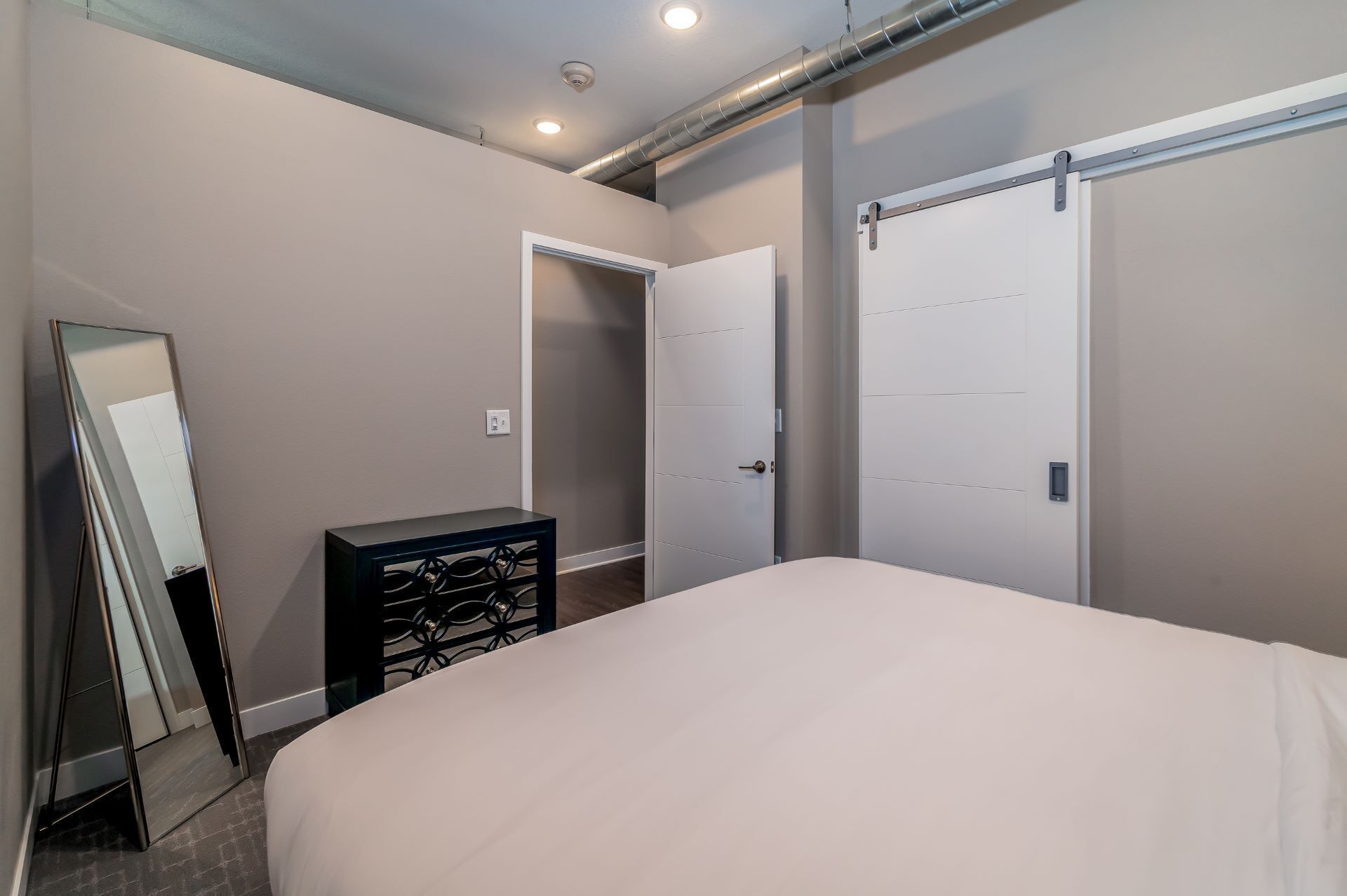 Une chambre à coucher avec un lit, une commode, un miroir et deux portes.