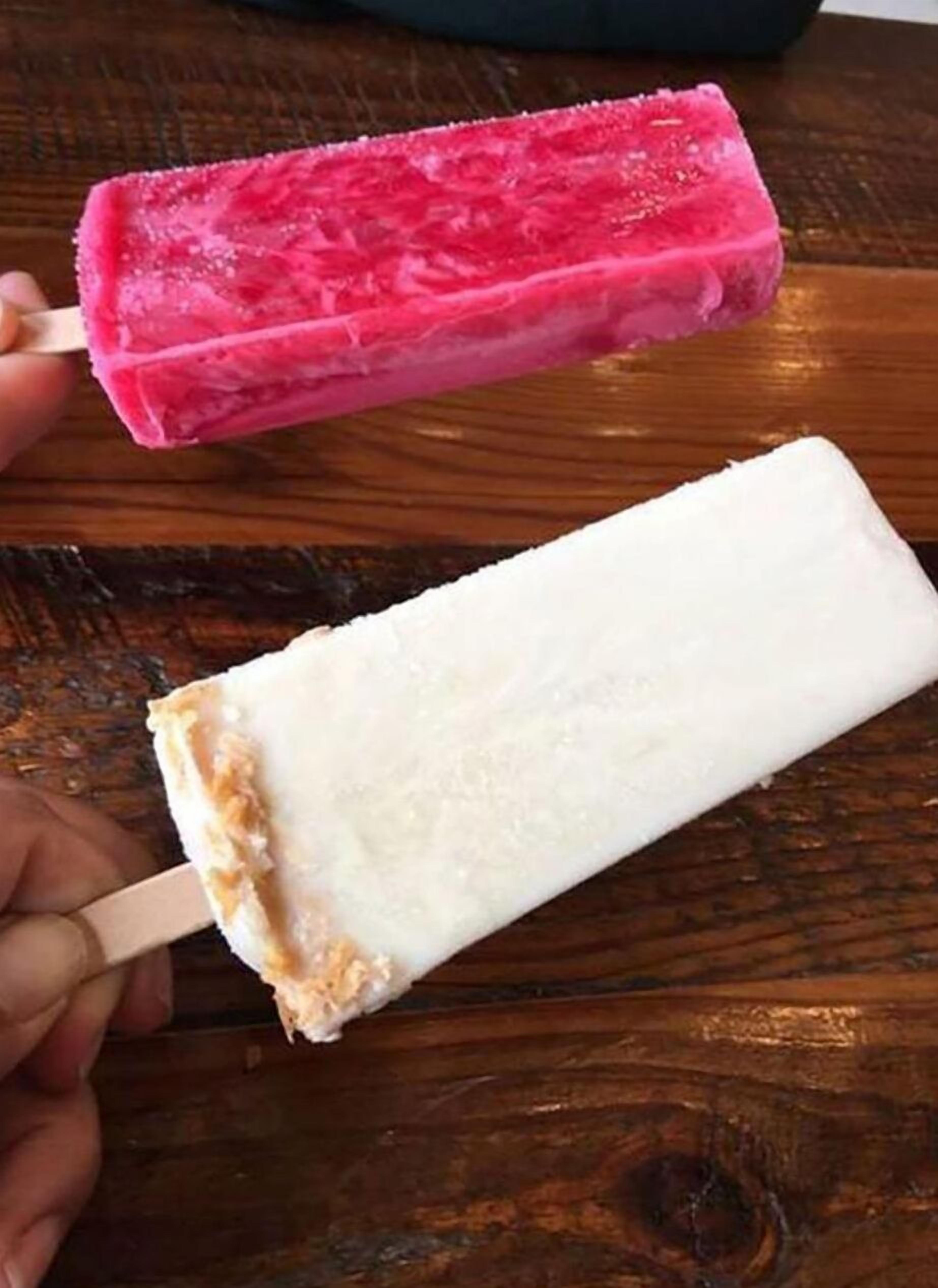 Dos polos de helado, uno rosa y otro blanco, sobre una superficie de madera.