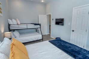 A room with bunk beds, a flat bed, a TV, and a door.