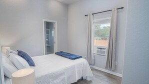 A bedroom with a bed, bedside lamp, and a view of the outdoors through a window.