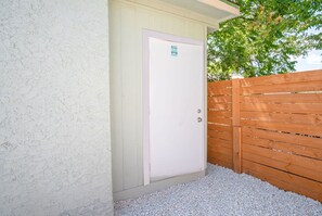 A white door with a small sign, a wooden fence, and a gravel ground. - Cozy and Lovely 2BR 2BA Apt A Near Lively Downtown (San Antonio)