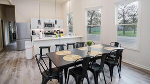 A modern kitchen with white cabinets, a stainless steel refrigerator, and a central island with bar stools. - Magnificent 4BR Near Famous Riverwalk and Downtown (San Antonio)