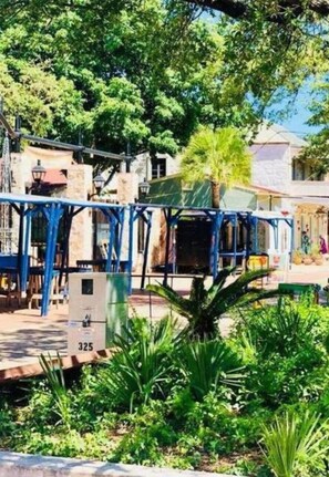 A courtyard with a blue metal structure, a building with a tiled roof, and lush greenery. - Stunning Cozy Downtown Guesthouse (San Antonio)