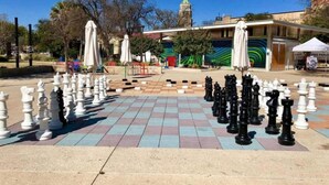 Un tablero de ajedrez grande al aire libre montado en una plaza pública, con un edificio de fondo.