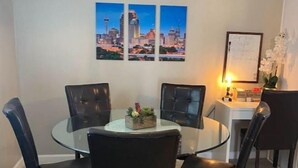 Un comedor con una mesa redonda de vidrio, sillas negras, una lámpara colgante y un mural con vistas a la ciudad.