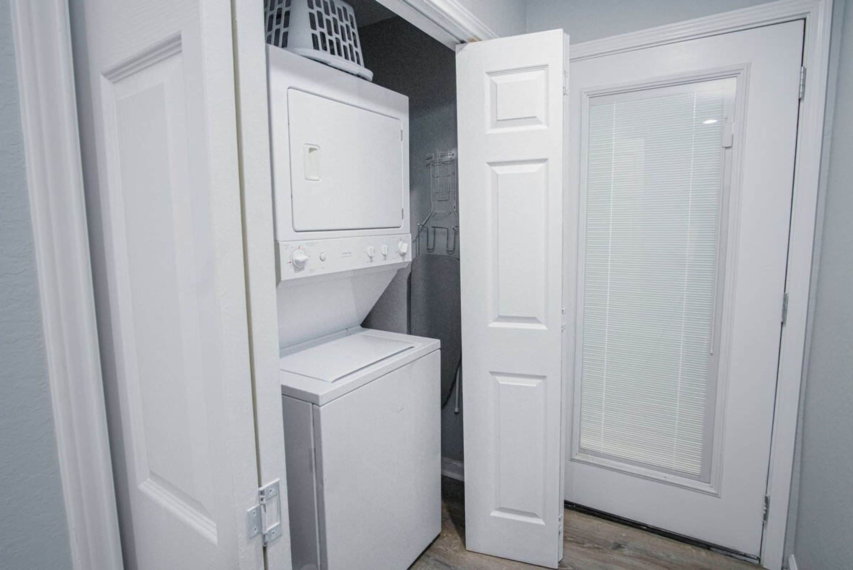 A laundry room with stacked washers and dryers, a door with a window, and a basket on the top washer.