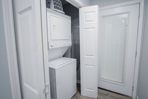 A laundry room with stacked washers and dryers, a door with a window, and a basket on the top washer. - Exceptional 5BR So Close to Riverwalk and Downtown (San Antonio)