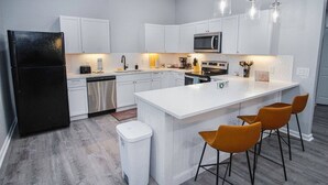 Una cucina moderna con mobili bianchi, un frigorifero nero, un forno a microonde e un'isola centrale con sgabelli da bar.