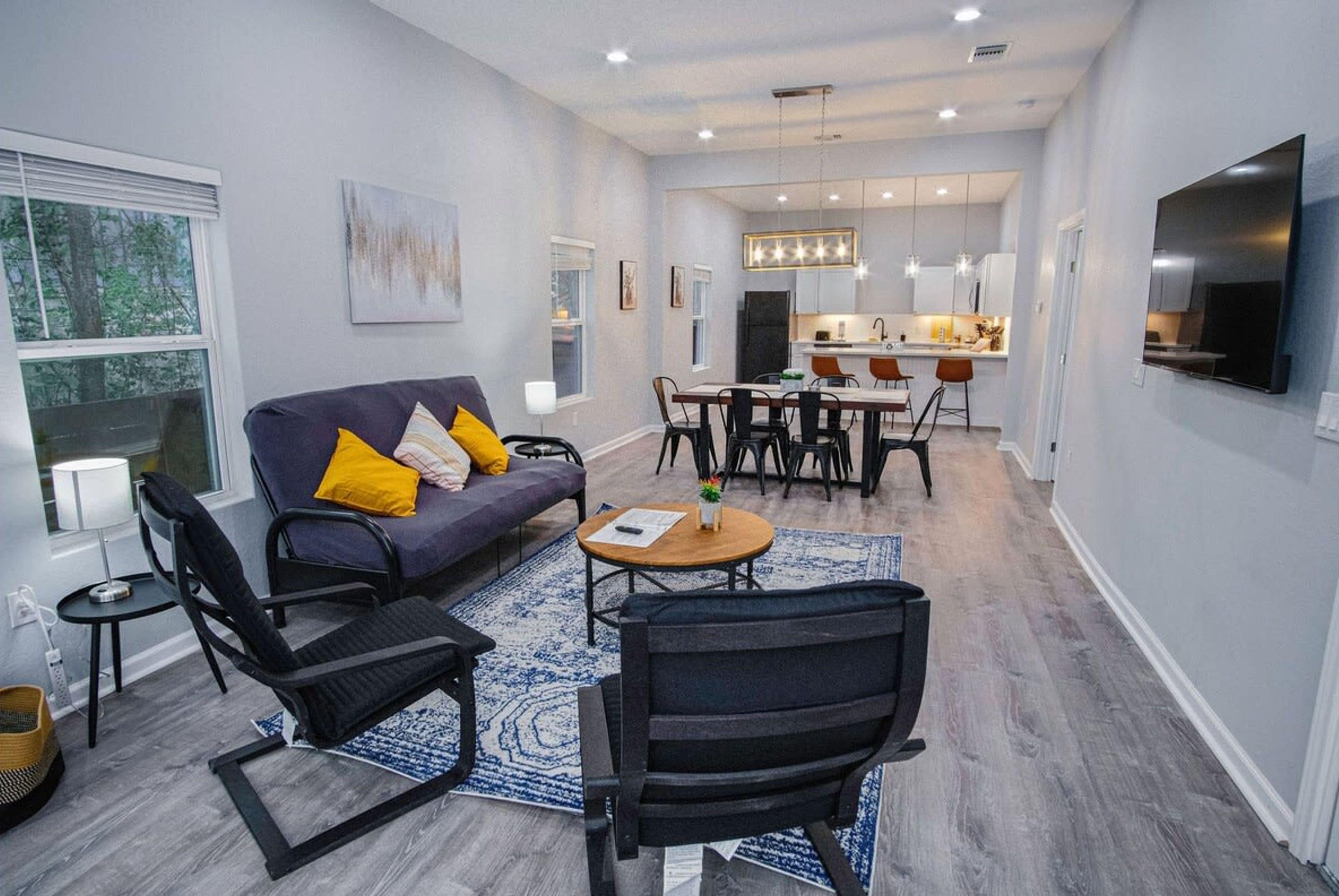 A modern living room with a sofa, chairs, a coffee table, and a dining area with a kitchen in the background.