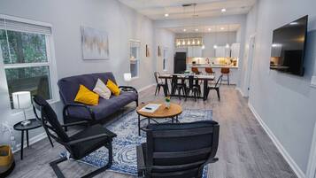 A modern living room with a sofa, chairs, a coffee table, and a dining area with a kitchen in the background.