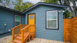 A two-story house with a wooden staircase leading to the front door, a small porch, and a fenced yard. - Exceptional 5BR So Close to Riverwalk and Downtown (San Antonio)
