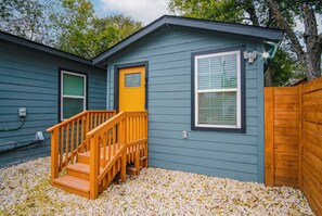 A two-story house with a wooden staircase leading to the front door, a small porch, and a fenced yard. - Exceptional 5BR So Close to Riverwalk and Downtown (San Antonio)
