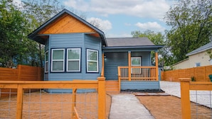 A small house with a porch, a fenced yard, and a clear sky. - Exceptional 5BR So Close to Riverwalk and Downtown (San Antonio)