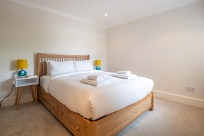 A neatly made bed with white linens and two pillows, flanked by two bedside tables with lamps, in a simple room with a carpeted floor. - Putney Perfection (London)