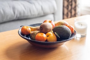 A bowl of fruits on a wooden table with a glass of milk beside it.