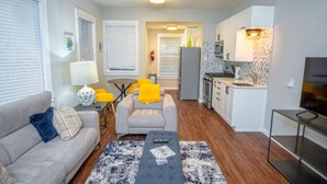 A living room with a sofa, coffee table, and a dining area with chairs. There is a kitchen with a refrigerator, stove, and microwave. - Remodeled Modern 1BR 1BA Apt Near Downtown 5min Pearl (San Antonio)