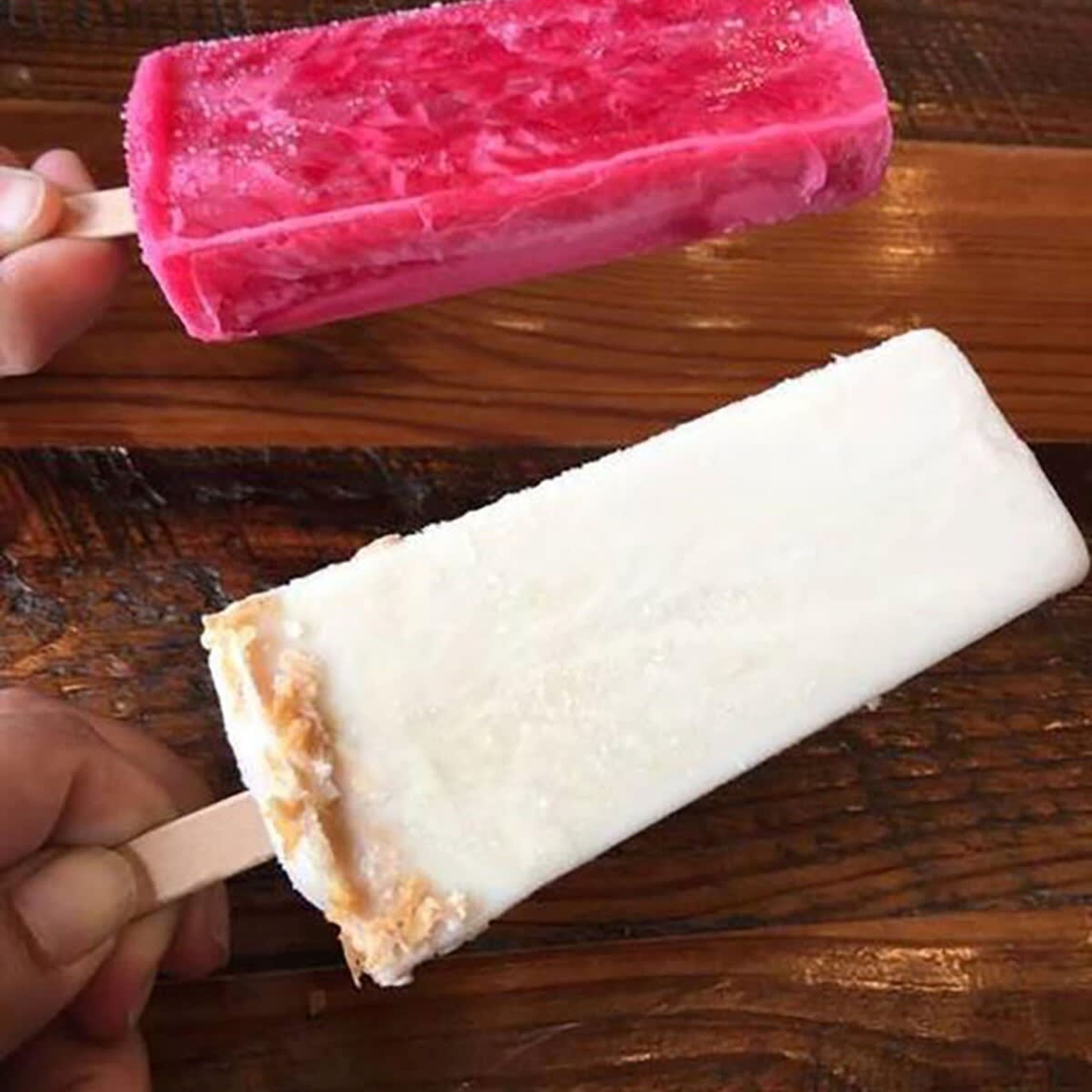 Una superficie de madera con dos helados, uno rosa y otro blanco.