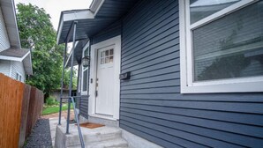 A residential house with a dark siding exterior, a white front door, and a small front porch with steps leading to the entrance. - Remodeled Modern 1BR 1BA Apt Near Downtown 5min Pearl (San Antonio)