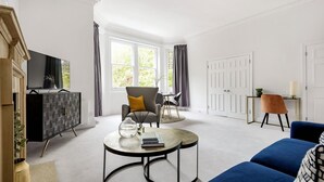 A modern living room with a large TV, a sofa, a coffee table, and a dining area. - The Belgravia Suite Next to Sloane Square (London)