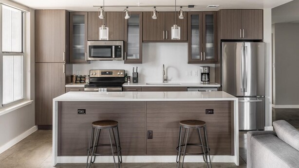 Een moderne keuken met een centraal eiland, roestvrijstalen apparatuur en barstoelen.