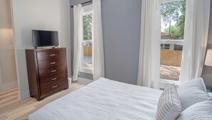 A bedroom with a bed, a dresser, a TV, and two windows with curtains. - Incredible New 3BR 2BA Near Downtown (San Antonio)