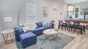 A modern living room with a blue sectional sofa, a round coffee table, and a dining area with a wooden table and chairs. - Incredible New 3BR 2BA Near Downtown (San Antonio)