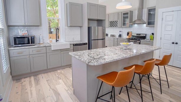 A modern kitchen with grey cabinets, a granite island, and a stainless steel refrigerator. - Incredible New 3BR 2BA Near Downtown (San Antonio)
