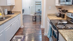A kitchen with granite countertops, white cabinets, a stove, and a microwave.