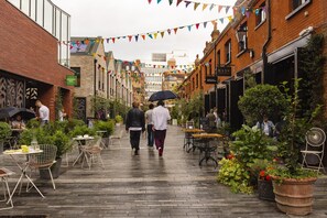 A narrow street lined with brick buildings, outdoor seating areas with tables and chairs, and potted plants. - The King s Road Suite Next to Sloane Square (London)