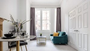 Un salon moderne avec une table à manger ronde, un canapé de couleur turquoise et une vue sur la ville grâce à de grandes fenêtres.