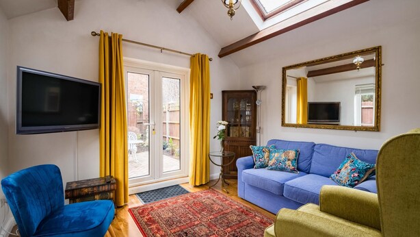 Ein Wohnzimmer mit einem blauen Sofa, einem gelben Sessel, einem roten Teppich mit Muster und einem großen Spiegel an der Wand.