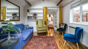 Ein Wohnzimmer mit einem blauen Sofa, einem grünen Sessel, einem roten Teppich mit Muster und einem Fenster mit Blick auf einen Holzzaun.
